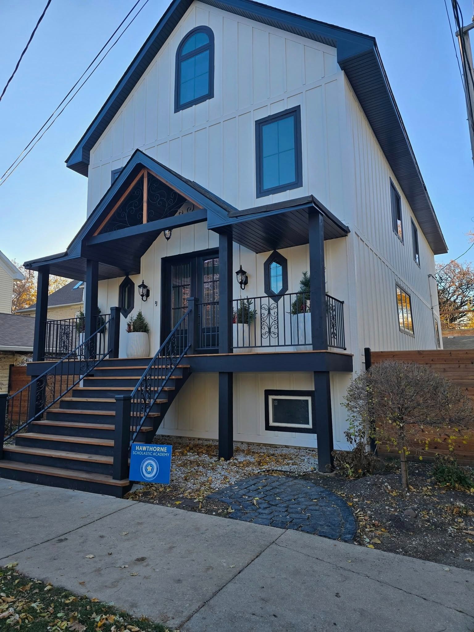 White two-story house with front porch, black stairs, and blue trim on a sunny street.
