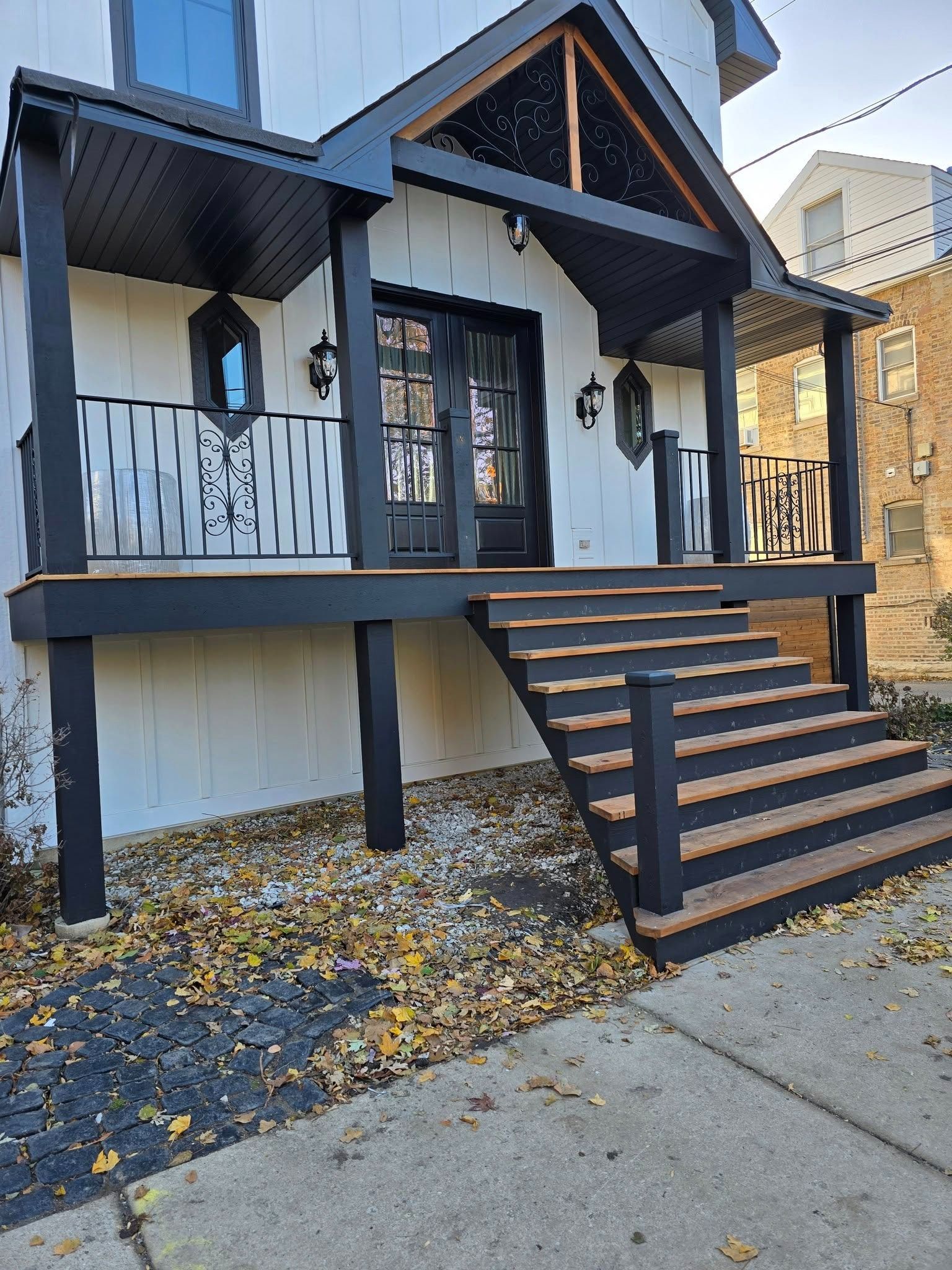 Front porch of a modern black-and-white house with stairs, railing, and leaf-covered ground