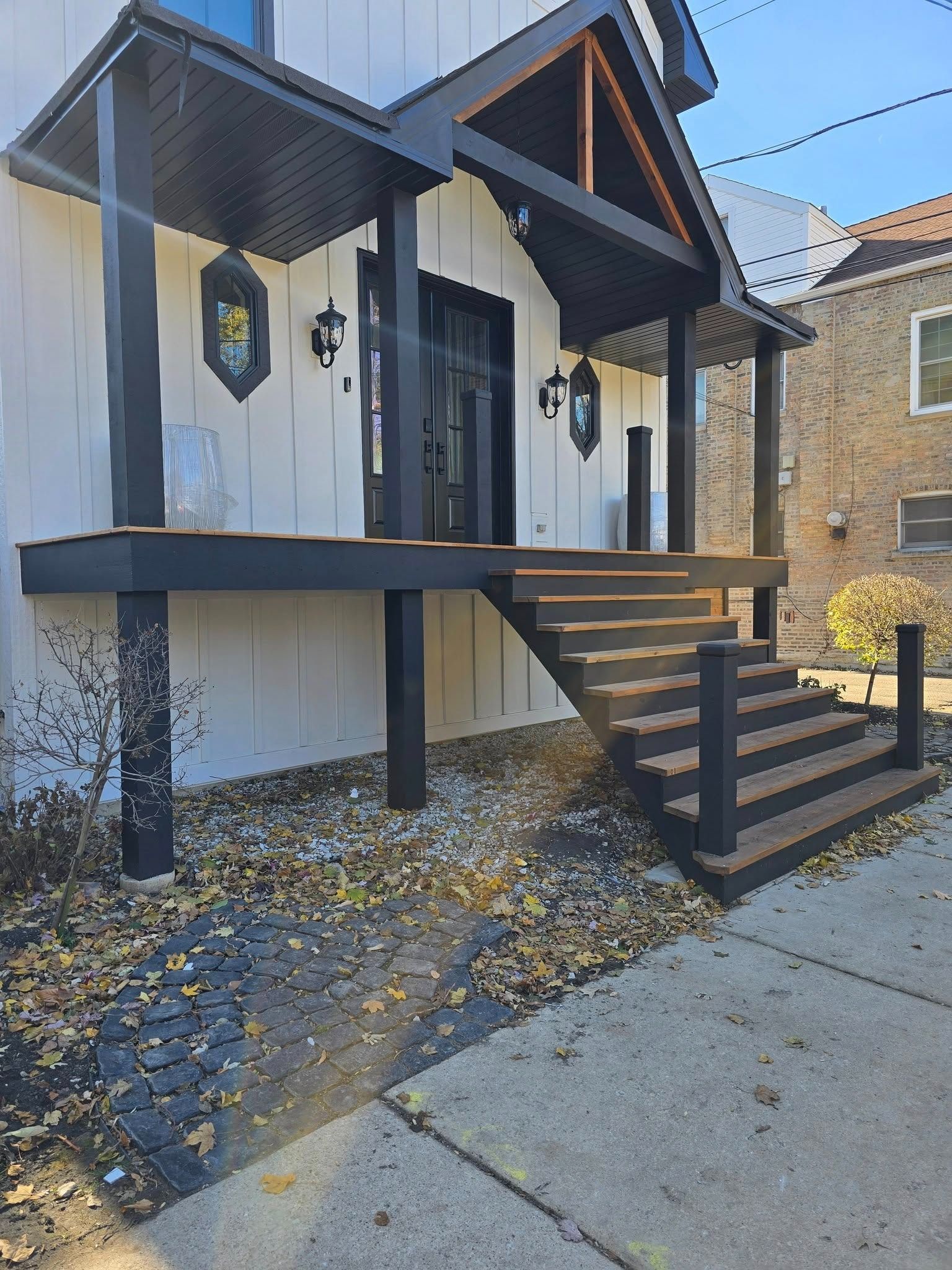 White house exterior with black trim, raised porch, and stairs by a stone walkway in autumn.