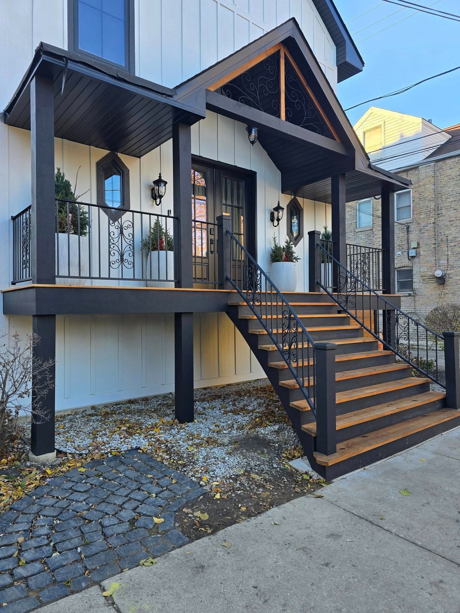 Modern house exterior with raised porch, black railings, and wooden stairs leading to the entrance