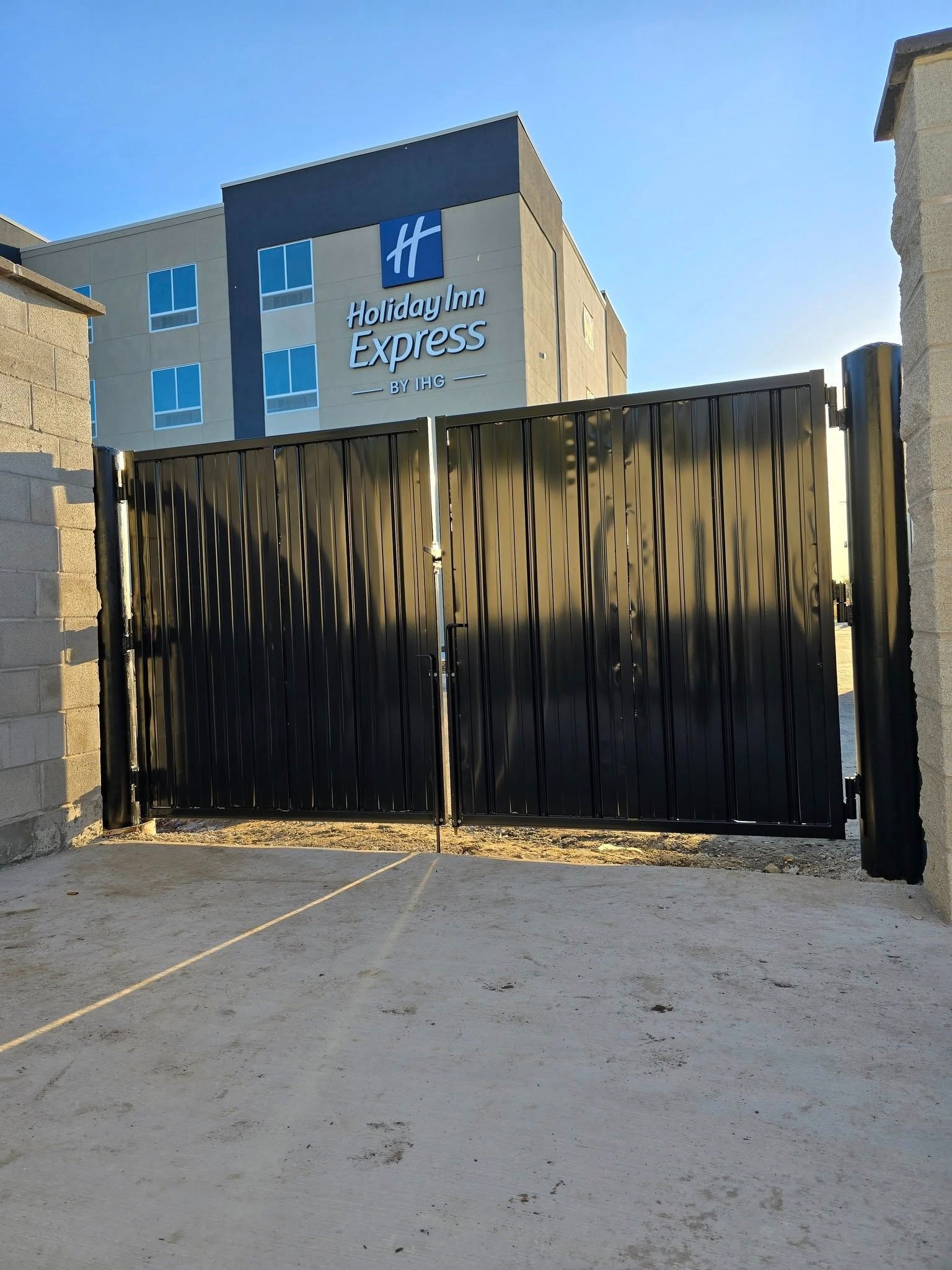 Black wooden gate in front of a Holiday Inn Express building and concrete driveway