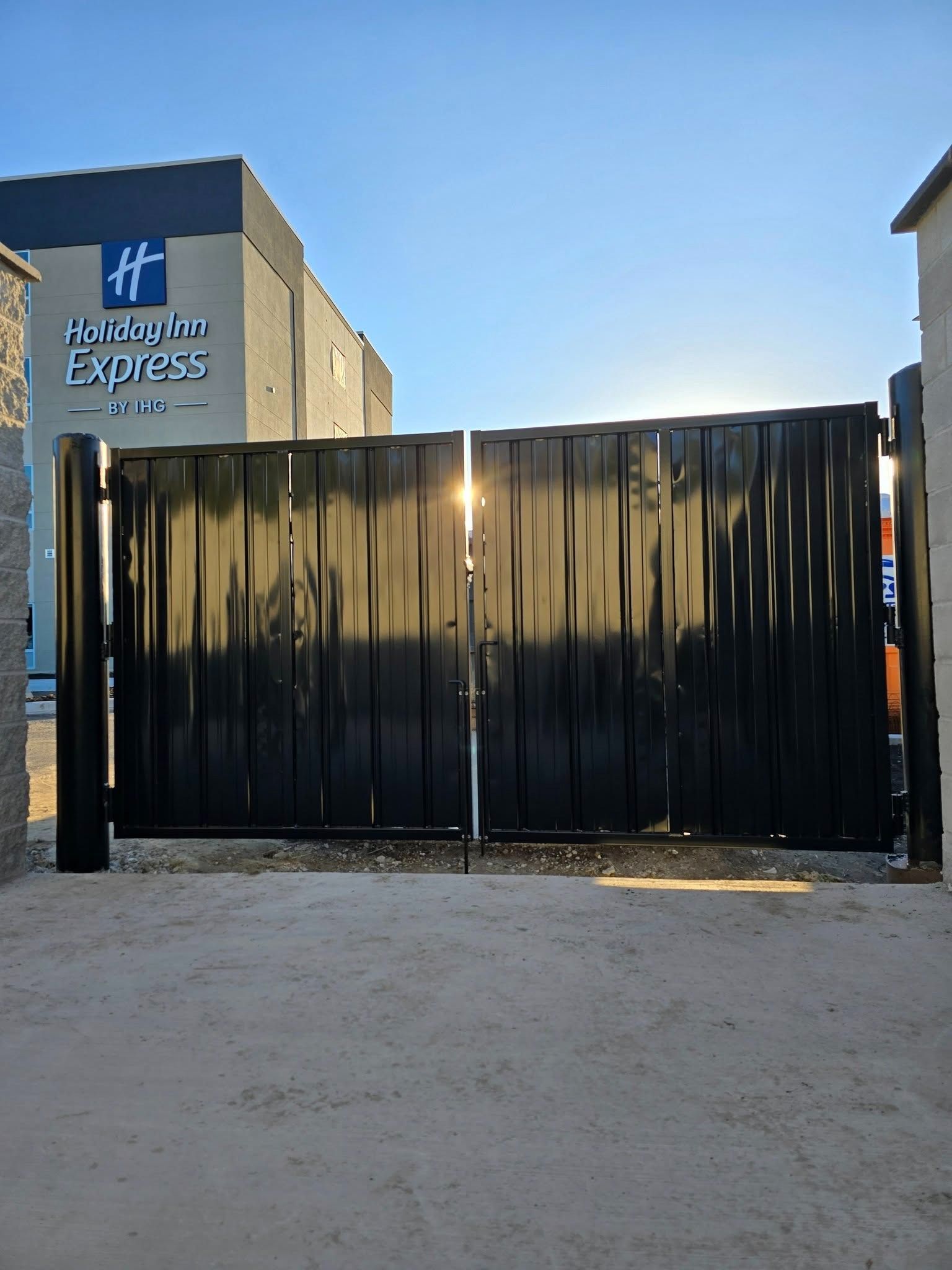 Black metal gate blocking the entrance to a Holiday Inn Express building under a clear sky