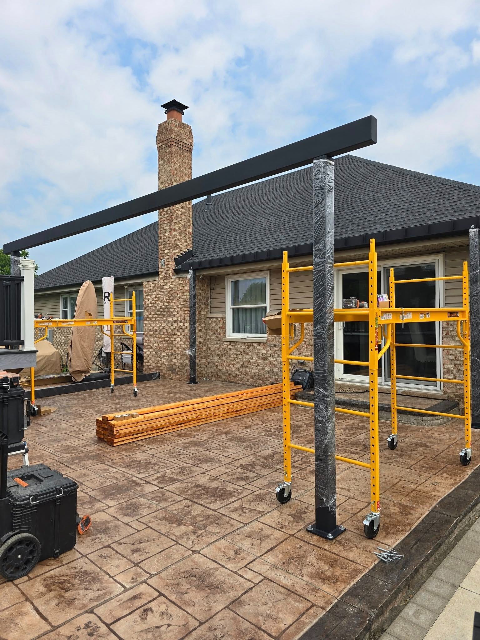 House exterior under construction with scaffolding, roof work, and stacked bricks in the front yard
