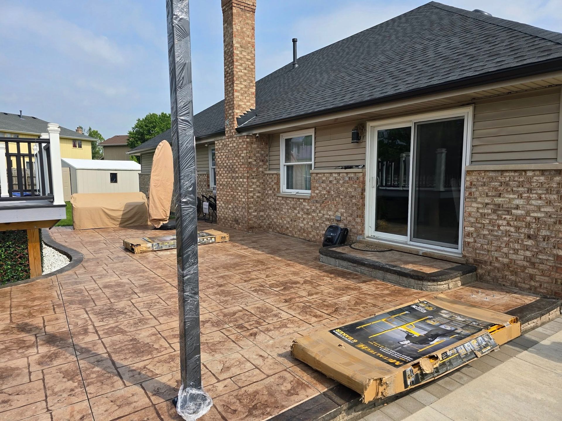 Patio with stamped concrete, sliding glass doors, and a vertical metal post beside a brick house