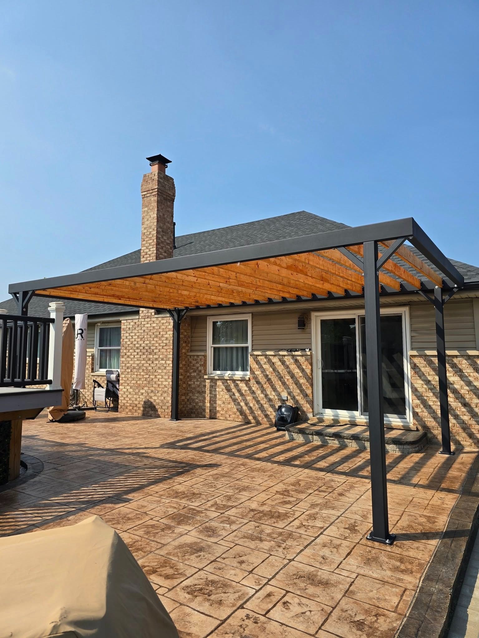 Back patio with brick house, pergola, and paved patio under a clear blue sky