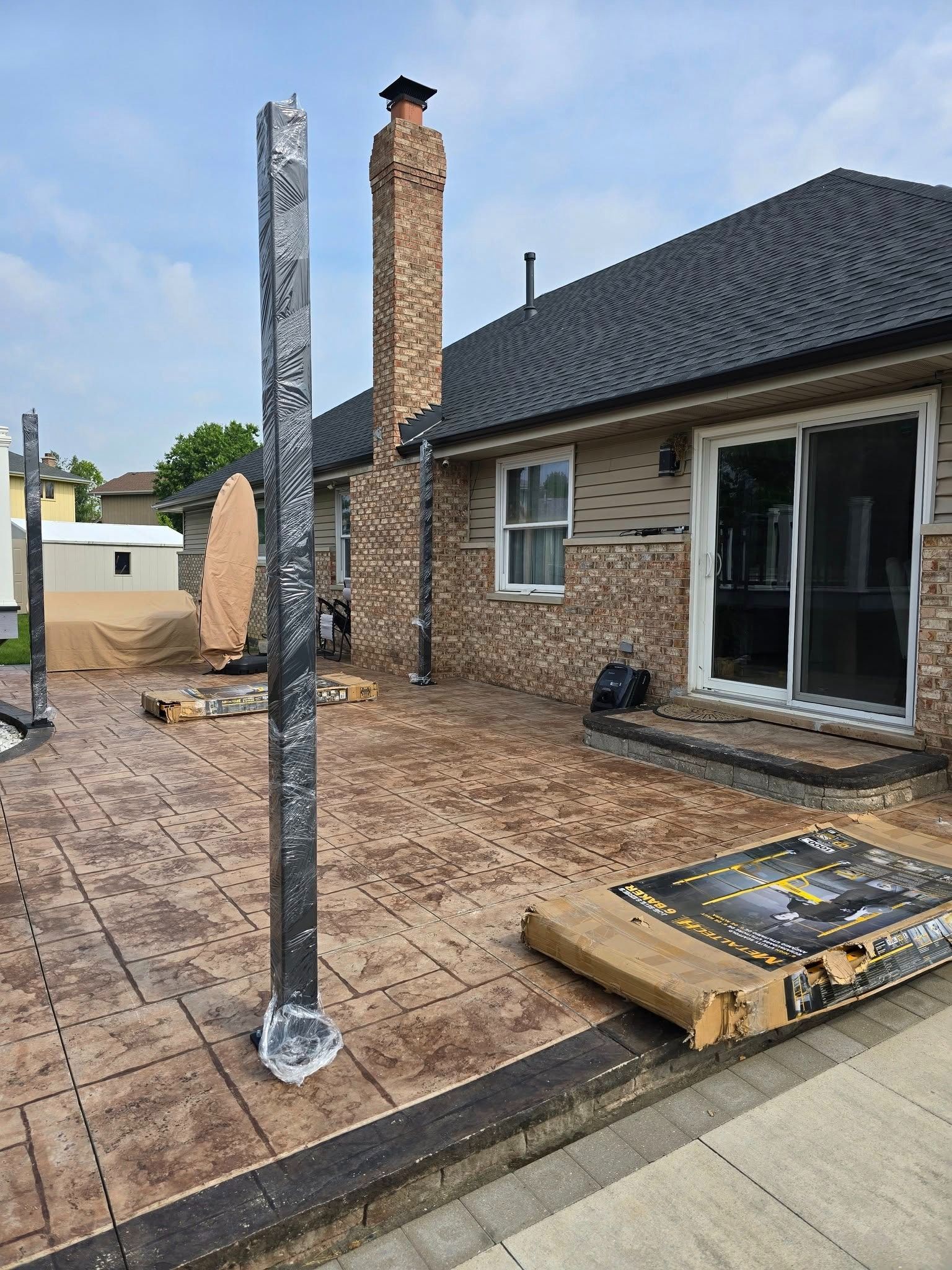 Backyard patio with a house wall, chimney, and a leaning metal post after apparent construction or damage
