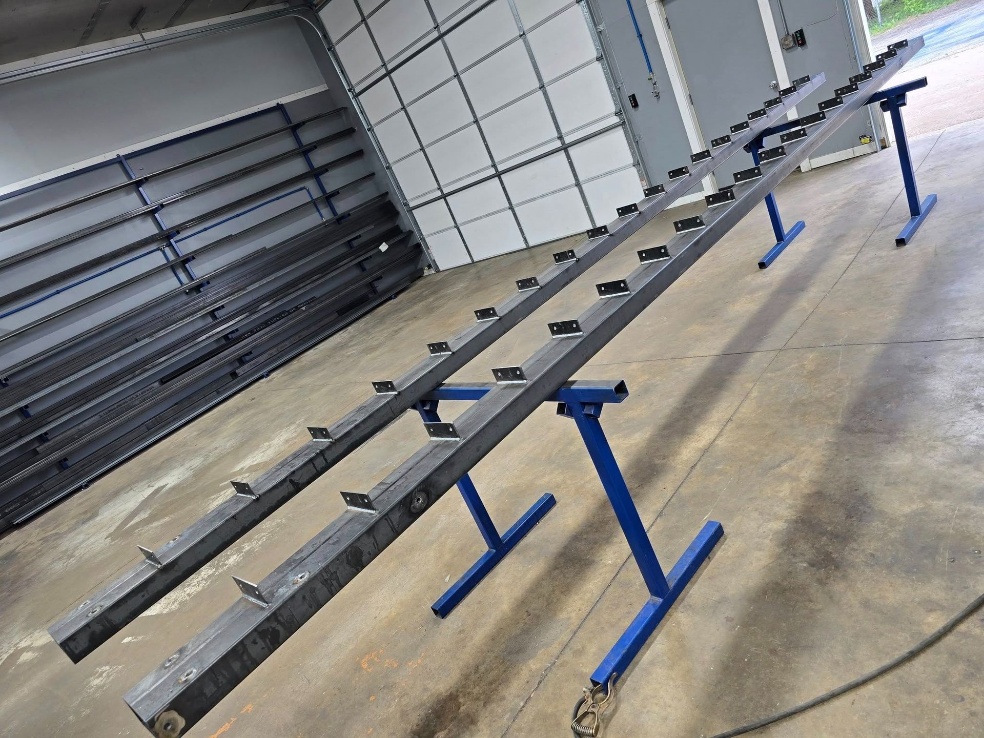 Metal frame on blue stands in a workshop, with black bars aligned along its length.