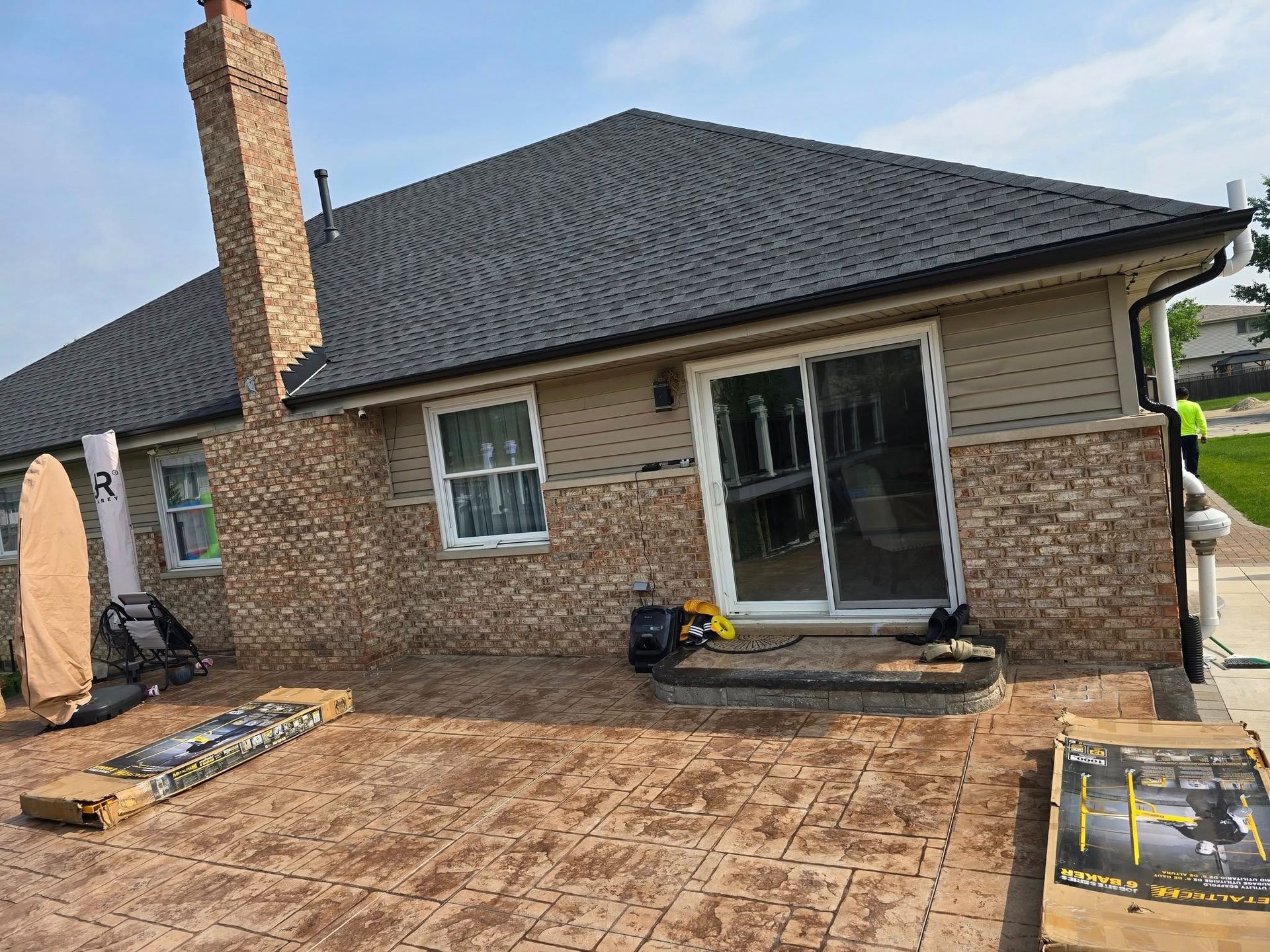 Backyard patio with a brick house, sliding glass door, chimney, and newly paved stone surface.
