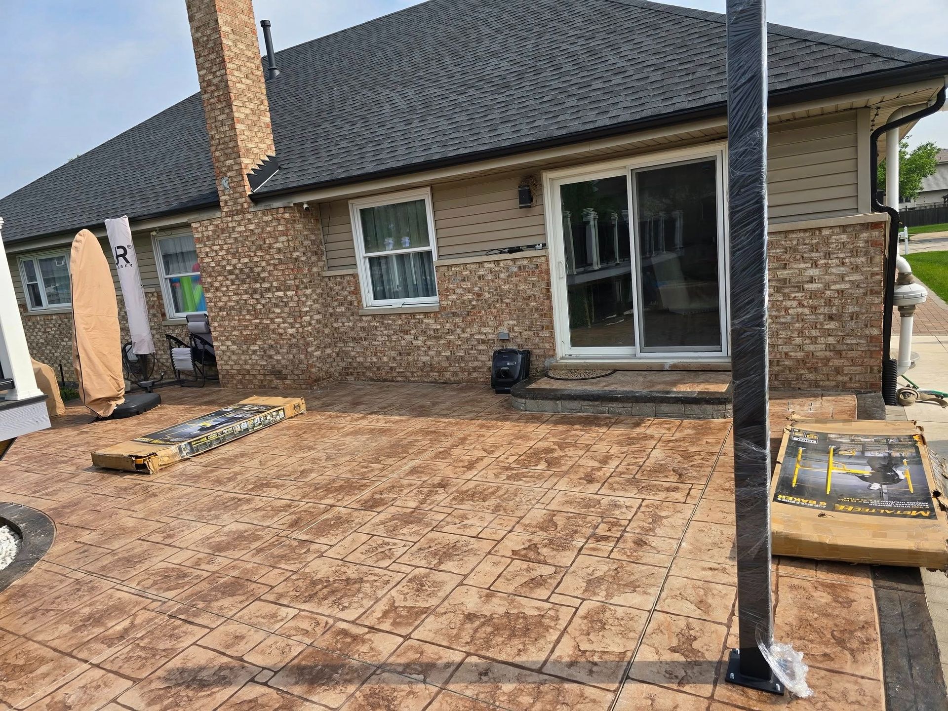 Backyard patio under construction with brick house, new paver flooring, and two black support posts