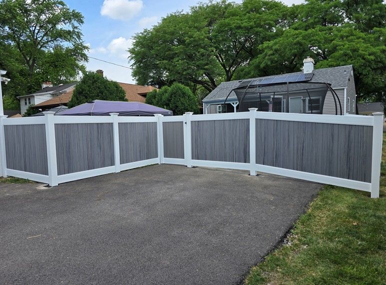 White vinyl fence with gray panels encloses a driveway and yard in a suburban neighborhood.