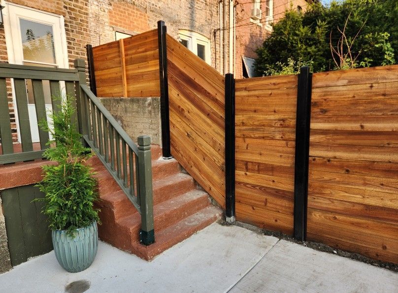 Brick stairway beside wooden fence with black posts and a potted plant on a concrete walkway