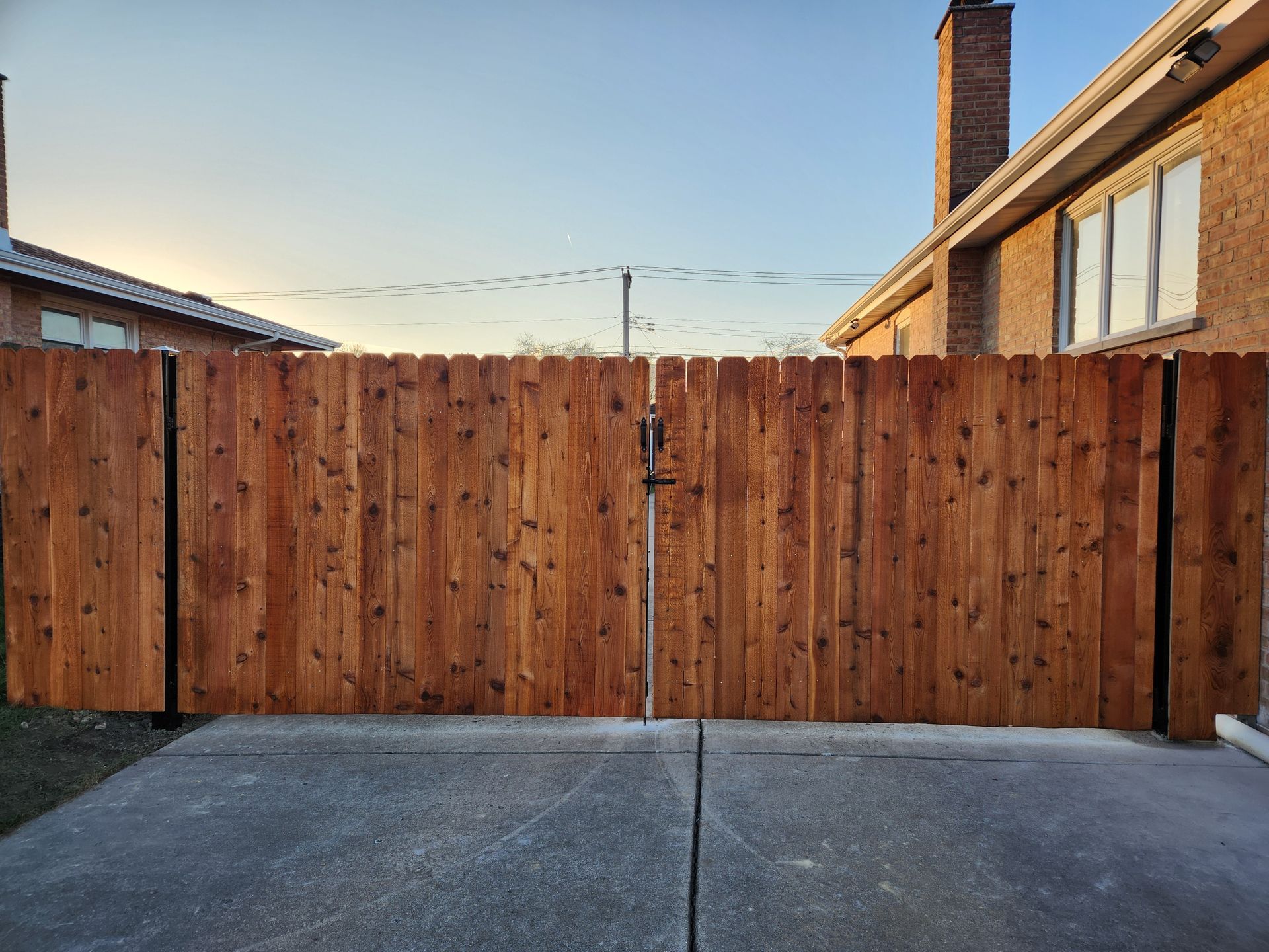 Wooden double gate across a driveway, with a concrete foreground and houses on either side.