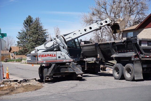 A crane is loading dirt into a dump truck.
