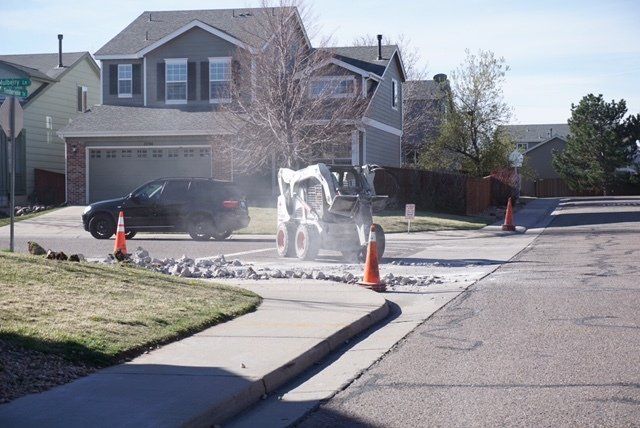 A bulldozer is cutting a hole in the sidewalk in front of a house.