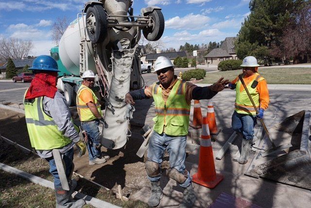 A group of construction workers are standing in front of a cement truck.