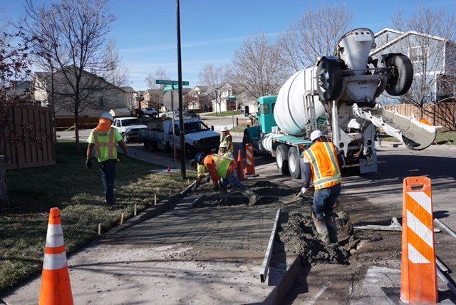 A group of construction workers are working on a sidewalk next to a concrete mixer truck.