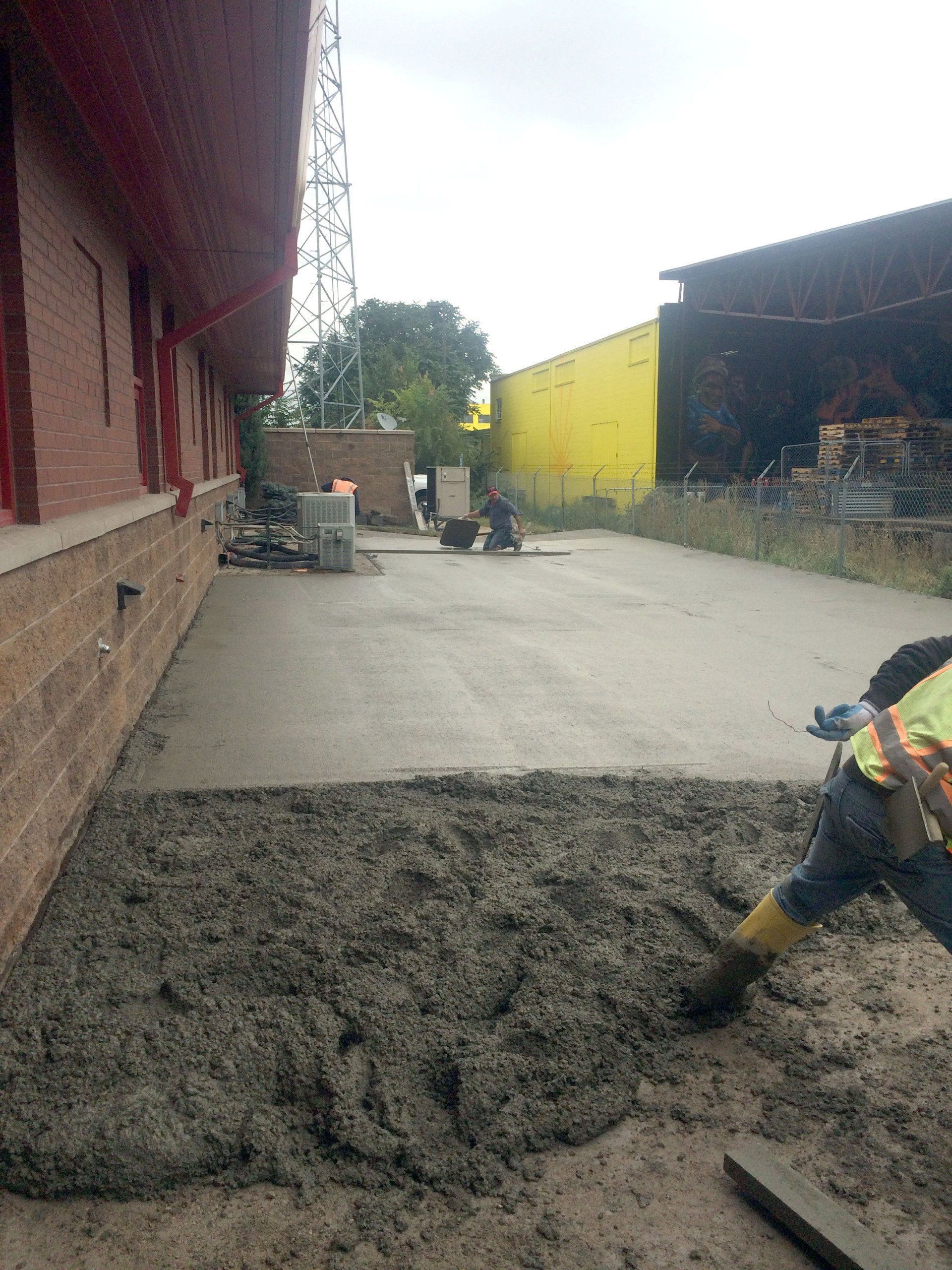 A construction worker is pouring concrete into a driveway.