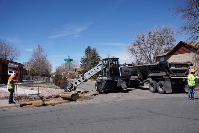 A couple of construction workers are standing next to a dump truck.