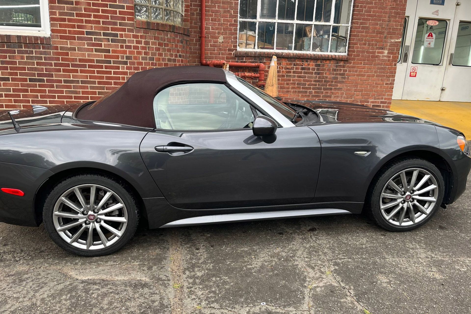 Dark gray convertible parked beside a brick building on wet pavement