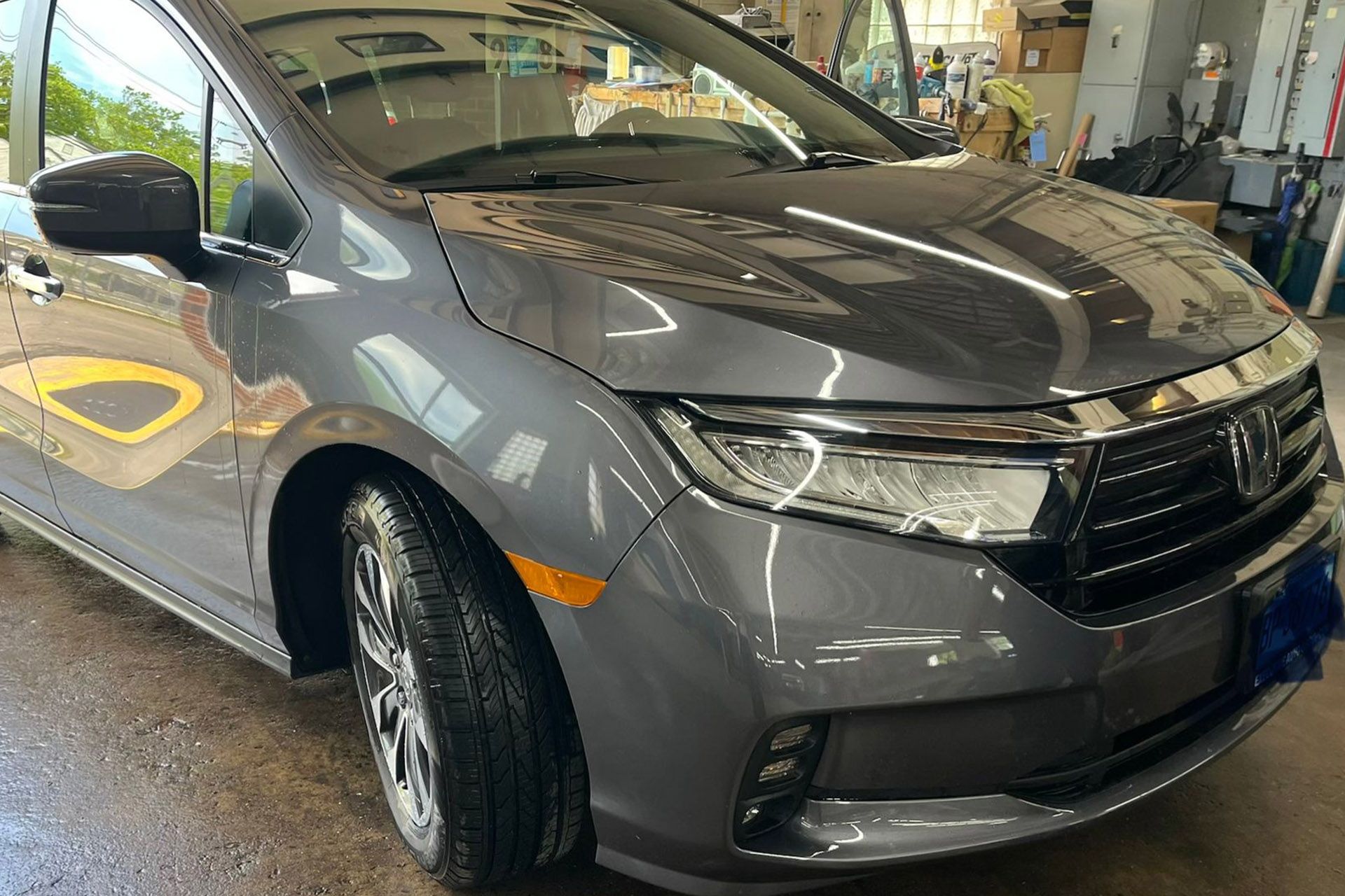 Gray SUV in an auto repair shop, front-left view with visible body damage and a dented hood