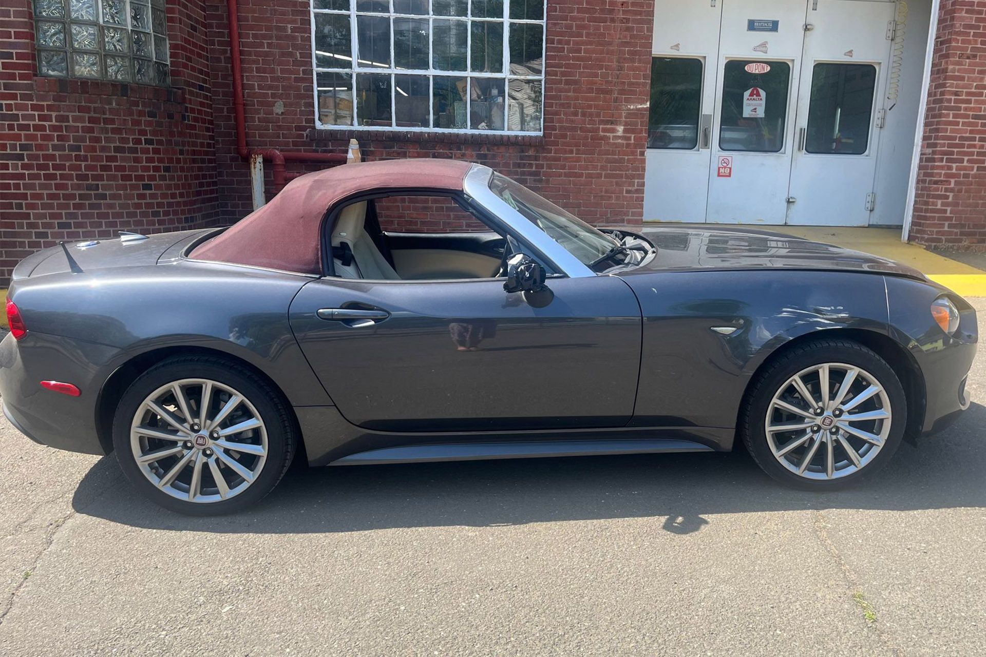Dark gray convertible sports car with a burgundy soft top parked by a brick building