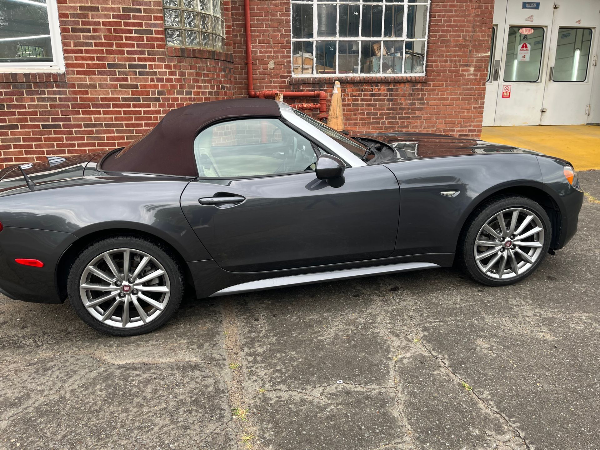 Dark gray convertible sports car parked beside a brick building.