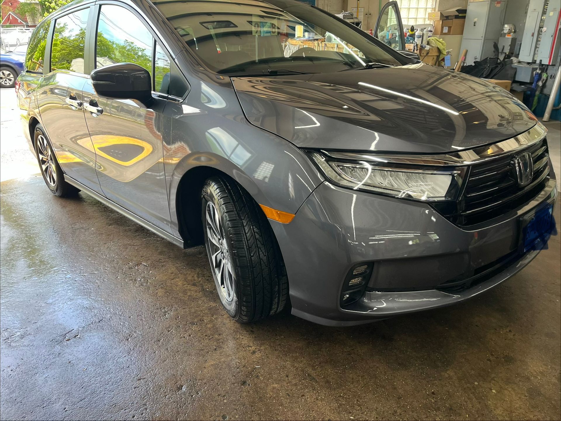 Gray minivan in an auto shop, shown from the front-left with headlights and grille visible