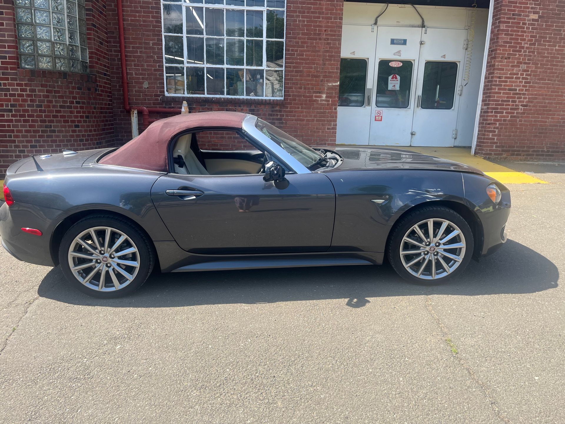 Gray convertible parked outside a brick building with red top down and black interior