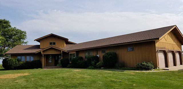 A large house with a brown roof is sitting on top of a lush green field.