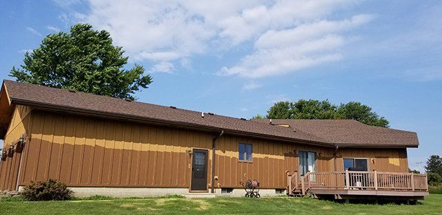 A large brown house with a deck and a blue sky in the background.