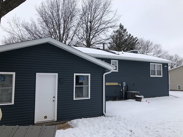 A blue house with a white door and windows is covered in snow.