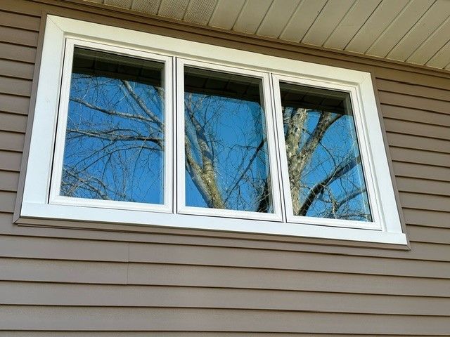 A window on the side of a house with trees reflected in it