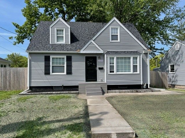 A small gray house with a concrete walkway leading to it.