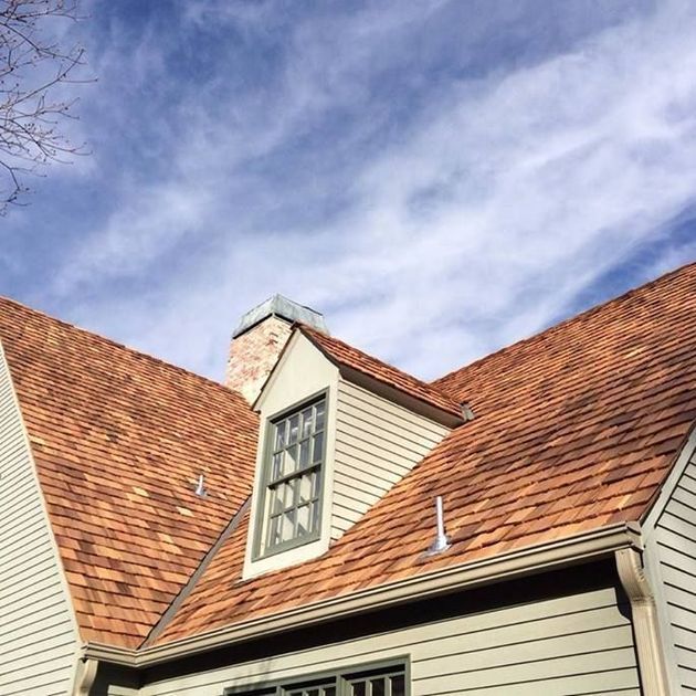 Red shingled roof with a dormer window against a blue, cloudy sky