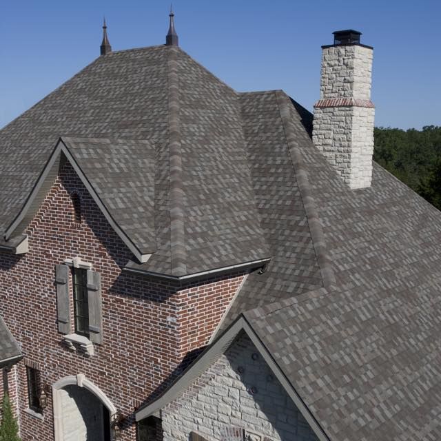 Brick house roof with gray shingles and white chimney against a blue sky