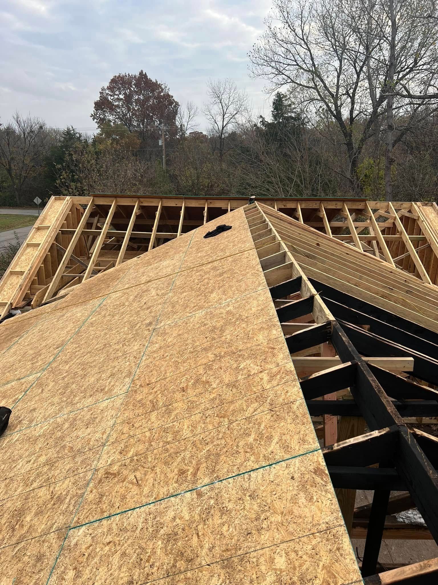 Roof under construction with plywood sheathing and exposed trusses against a cloudy sky