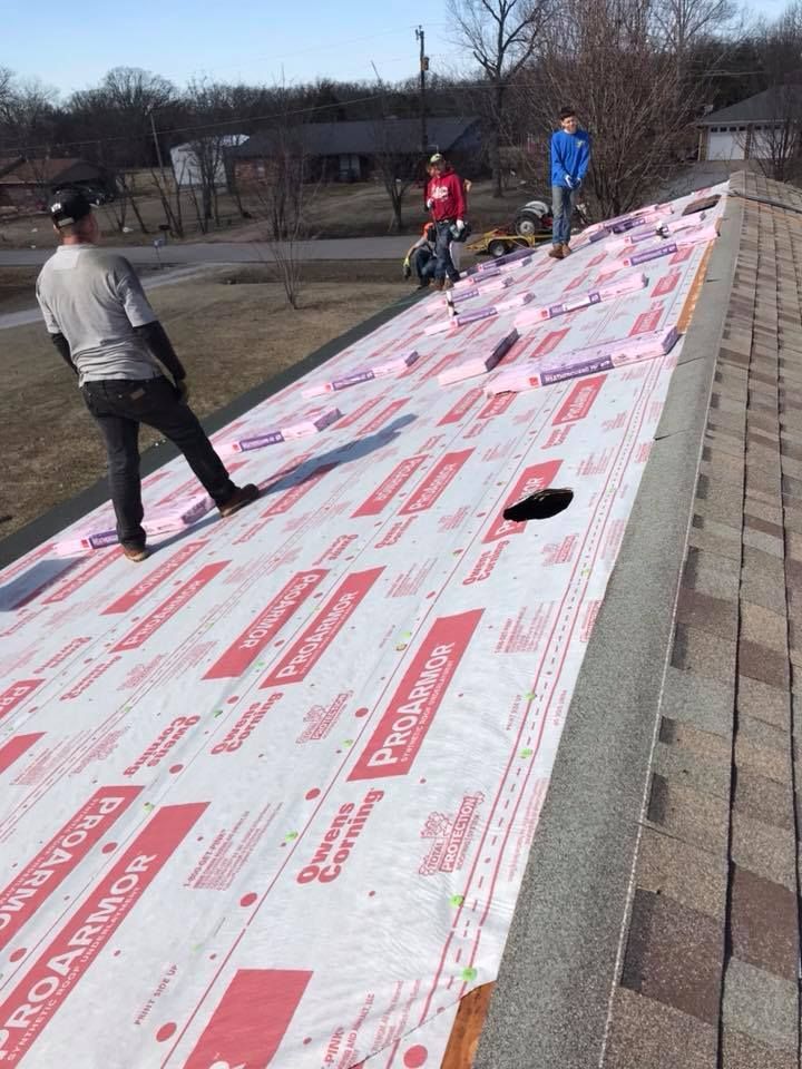 Workers laying white roof underlayment on a sloped roof in an outdoor yard
