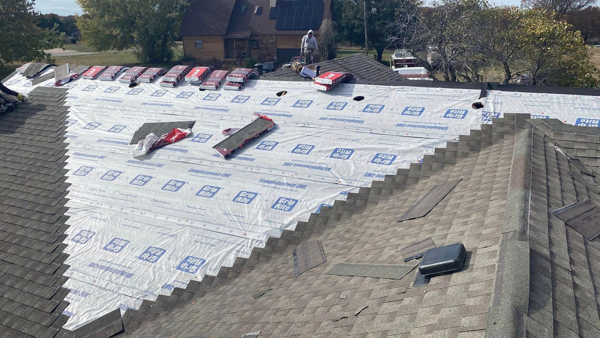 Rooftop under repair with white underlayment, tools scattered, and exposed gray shingles along one side.