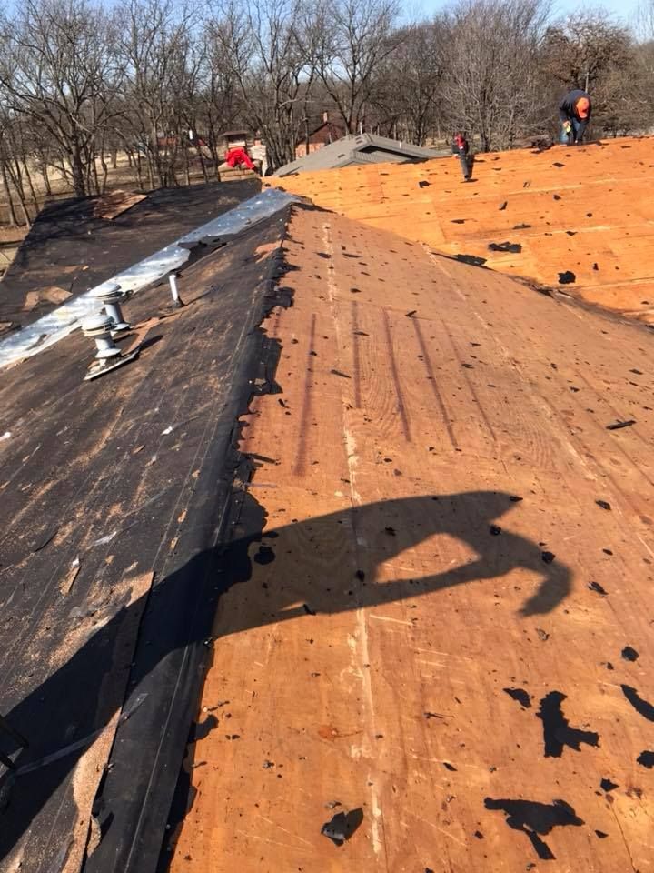 Roof under repair with workers on a partially stripped black and orange rooftop under a clear sky