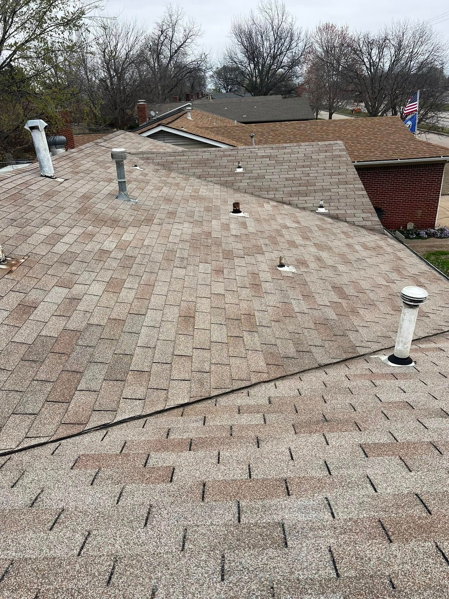 Rooftop with weathered gray shingles, several vent pipes, and a red brick chimney under cloudy sky.
