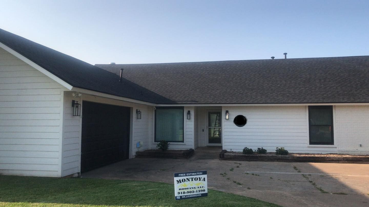 Single-story house with white siding, dark roof, front driveway, and a small yard sign.