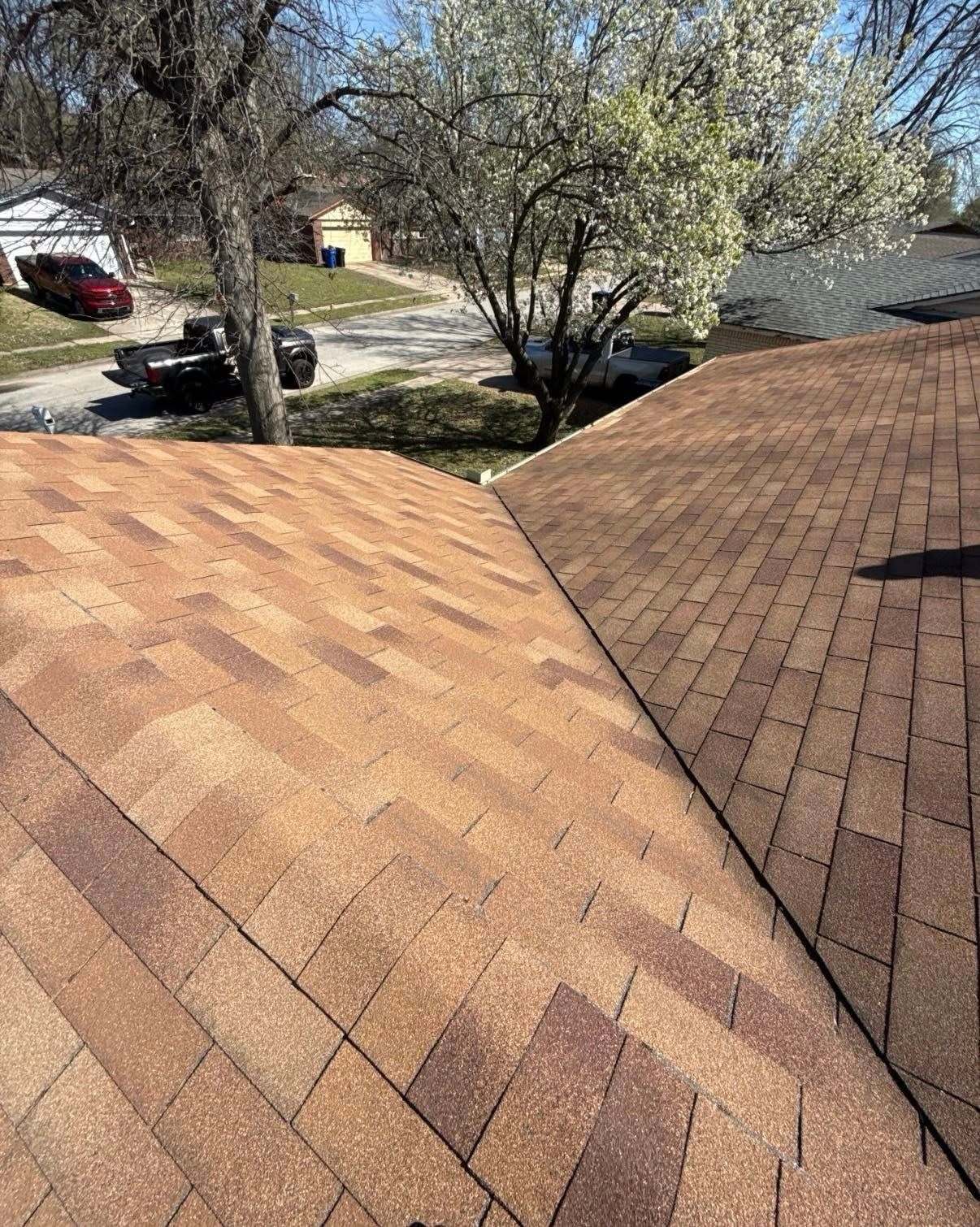Two adjacent shingled roof sections with trees, a driveway, and parked cars in the background