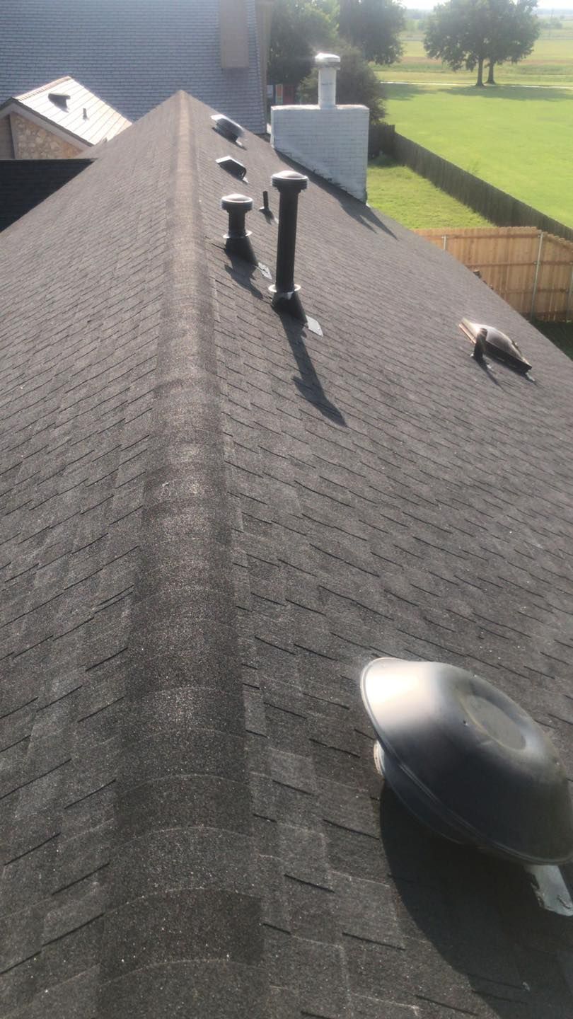 Rooftop with dark shingles, vents, and a skylight under a clear sky, viewed from above