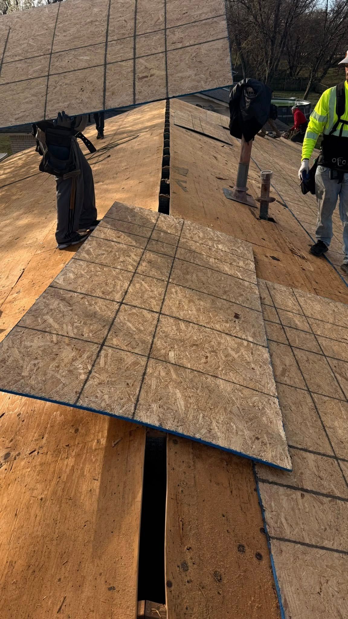 Workers installing roofing shingles on a steep roof, with one panel lifted open in the foreground.