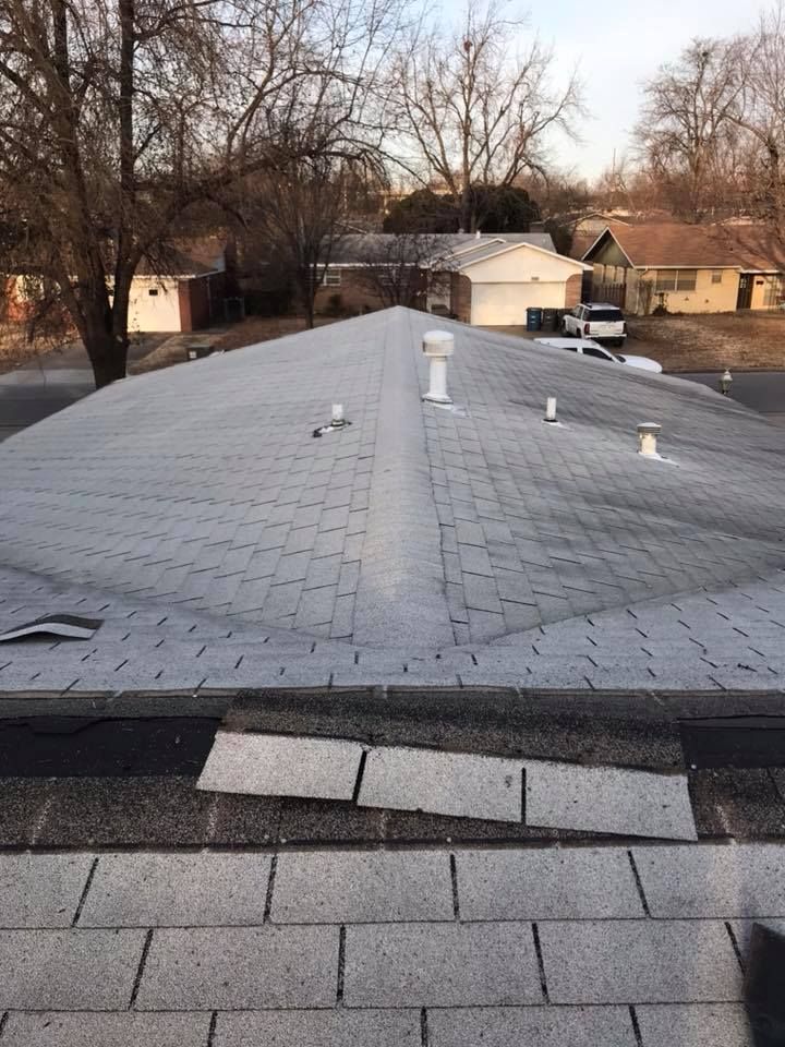 Gray shingled roof with several vents, viewed from above, with trees and houses in the background