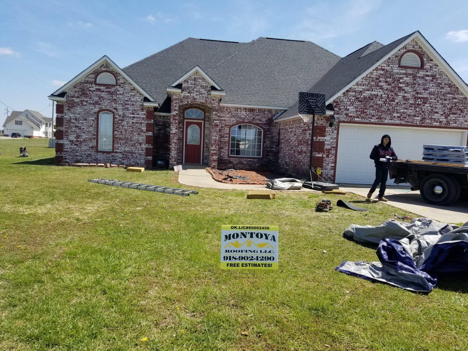 Brick house with gray roof, moving truck, and yard signs on a sunny day