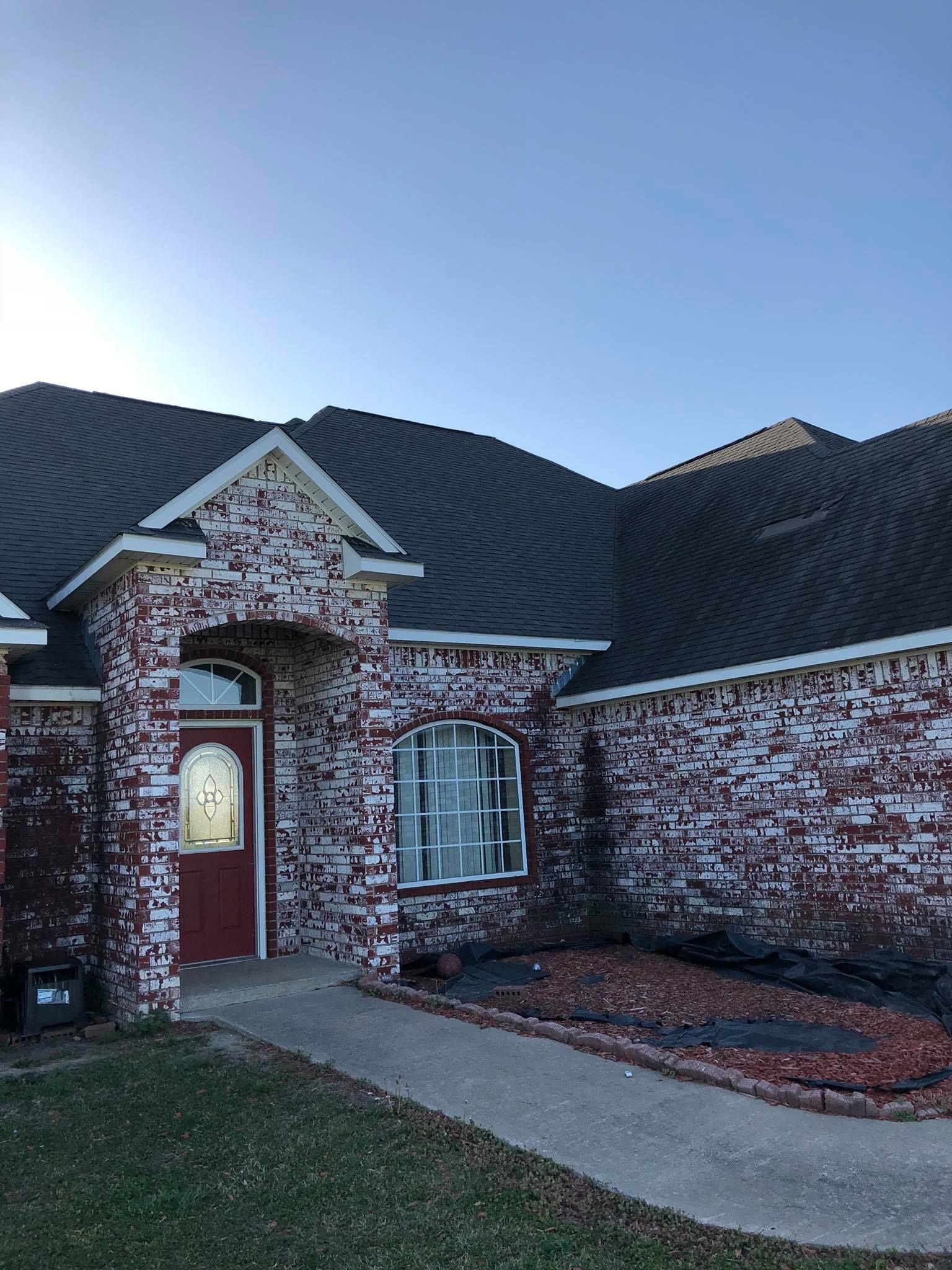 Brick house exterior with arched front door, patterned shingle roof, and curved walkway under a clear sky