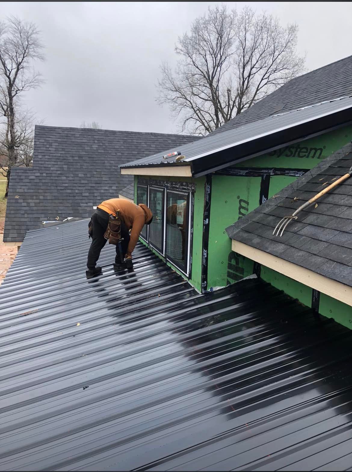 Worker installing black metal roofing on a house under construction