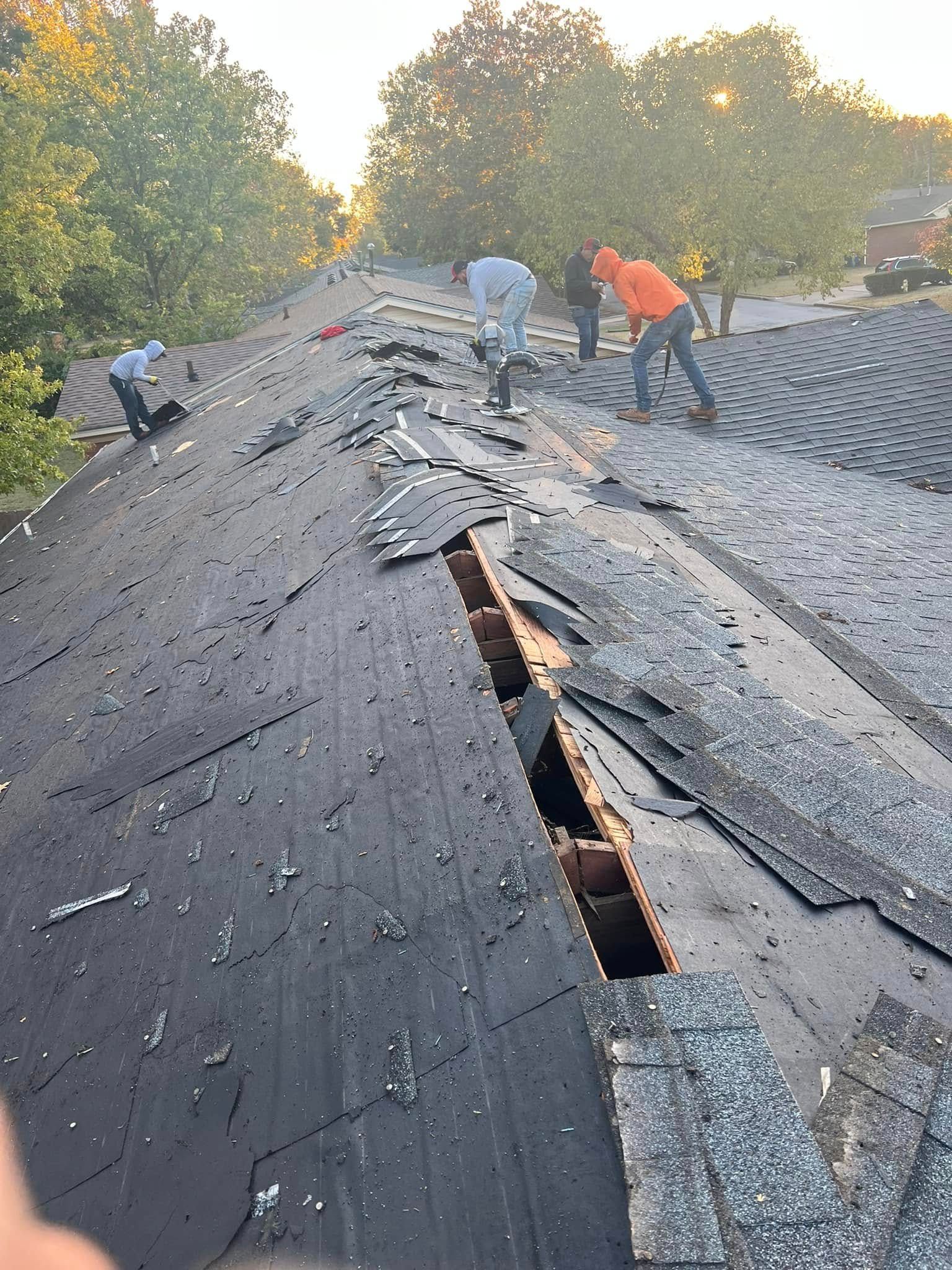 Workers repairing storm-damaged roof with missing shingles and exposed wooden opening at sunset