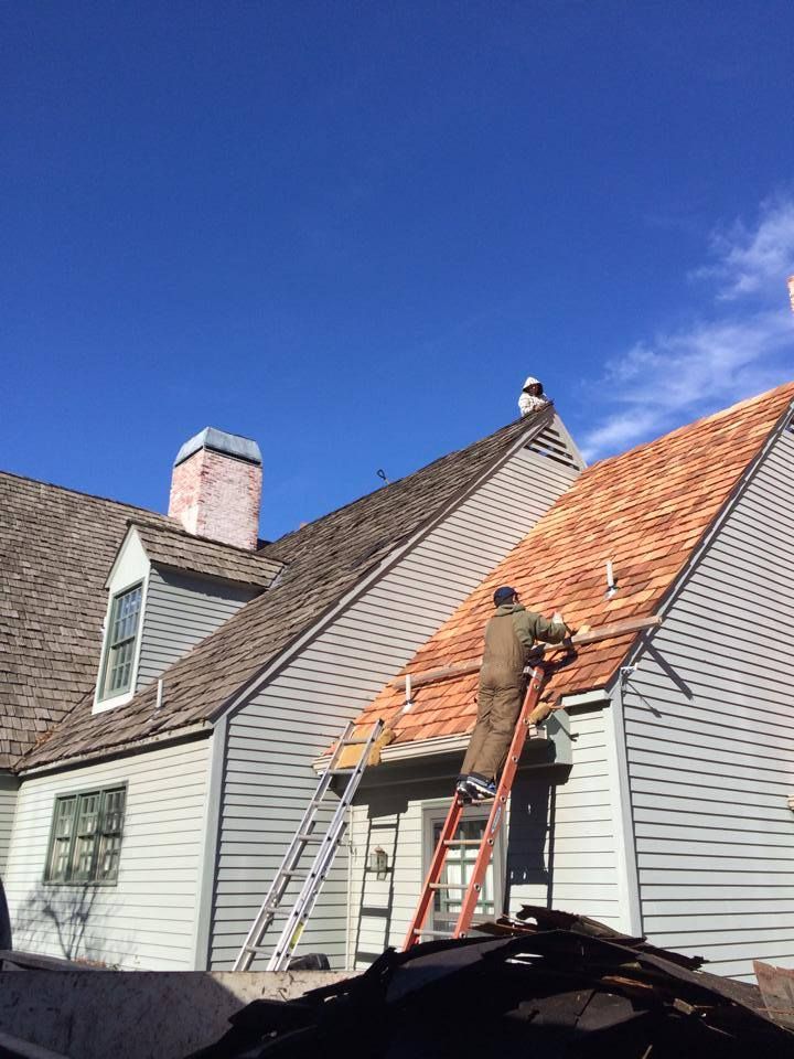 Worker on a ladder repairing the roof of a gray house under a clear blue sky